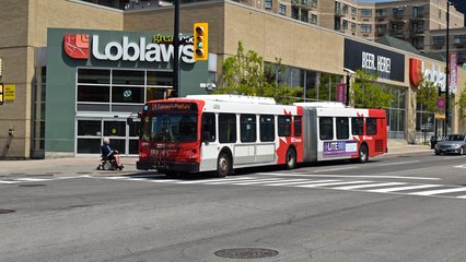 An OC Transpo New Flyer D60LFR services the bus stop at Rideau and Nelson Streets while running the 14 route to Tunney's Pasture before continuing on.