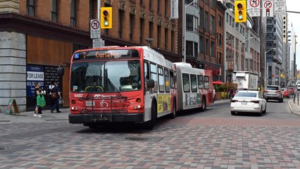 OC Transpo bus 6487, a New Flyer D60LFR, makes a left turn from Queen Street onto Bank Street while operating the 7 route.  OC Transpo is the name of the transit service in Ottawa, and includes a fairly extensive bus network, as well as the O-Train.