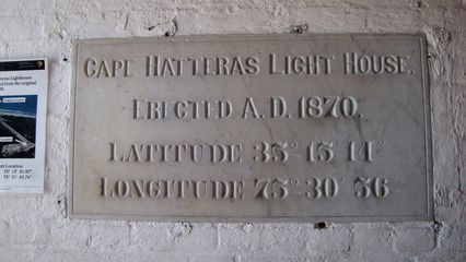 Plaque next to the entrance, showing the date the lighthouse was built, and the coordinates where it was originally located. The printed sign on the wall next to this marker shows the new coordinates following the lighthouse's 1999 relocation.