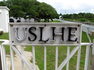 "USLHE" on a gate next to the lighthouse. USLHE stands for "United States Lighthouse Establishment", which originally operated the lighthouse. The lighthouse is now operated by the United States Coast Guard, as is also the case with Cape Hatteras.