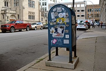 Mailbox covered in stickers, across Baum Blvd. from the church.