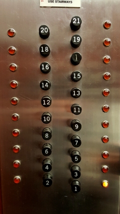 Buttons on the Investment Building elevator, with pop-out buttons and indicator lights to the sides of the buttons. The first floor is selected in the left photo.