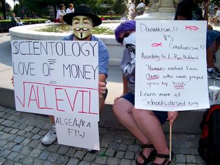 Enturb and Purple Hair Anon hold up their signs in our pre-raid meeting point at Dupont Circle. This would be the last raid where we went through the formality of meeting off-site before the raid and then marched the two blocks from Dupont Circle to the Org to make our appearance. Future raids would just meet up at the Org.