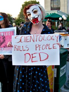 In keeping with the "undead" theme, Beret holds a sign saying, "Scientology kills people DED (sic)".