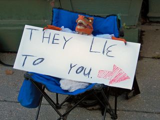 Raptor Jesus holds a sign saying, "They lie to you", with an arrow pointing at the Org.