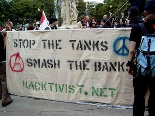 A group of people carried a banner with the URL for hacktivist.net, while also flying the Iraqi flag, as well as the red-and-black anarcho-syndicalist flag.