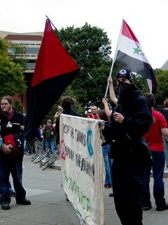 A group of people carried a banner with the URL for hacktivist.net, while also flying the Iraqi flag, as well as the red-and-black anarcho-syndicalist flag.