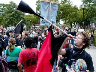 A man blows on a horn with the anarcho-syndicalist flag hanging from its shaft.