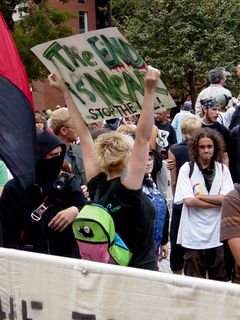 A woman holds her sign high from behind the Hacktivist banner.