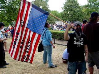 Black bloc demonstrators' statements took various forms. The gentleman on the left carries a flag, flown upside down (an international distress signal), with "smash the state" written on it. Another gentleman is dressed for battle, wearing a helmet, goggles, padding on both arms, and carrying an anarchist flag.