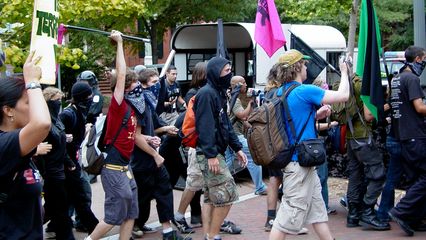 The black bloc marches past a row of Park Police officers in riot gear.