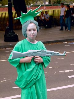 A girl dressed as the Statue of Liberty carries a toy machine gun.