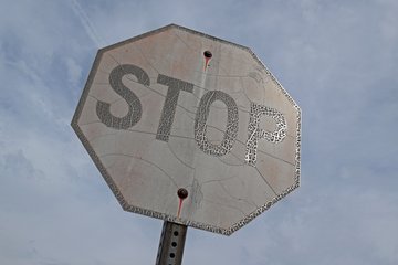 A very weathered stop sign in front of Sharp Shopper.