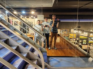 Group selfie on a mirrored wall on an upper level at an art gallery.