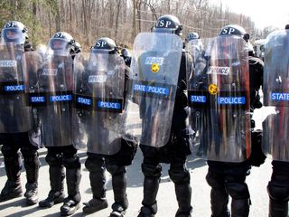 State Police in riot gear, with "Free Bradley Manning" stickers on their shields.