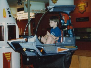 I celebrated my sixth birthday at Showbiz Pizza in Fayetteville, Arkansas. Here I am going up and down on one of their rides - some sort of spaceship.