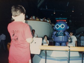 Near Spaceship Earth, at the CommuniCore attraction (which no longer exists), a I take my turn interacting with the robot seen in the distance, using a telephone handset.