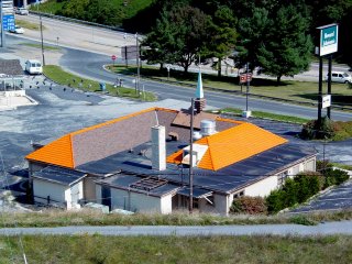 Next to the other buildings, the orange roof of the Howard Johnson's restaurant gleams brightly in the sun. Note how the orange tile only covers the outer portions of the roof. Presumably it was cheaper to do the inside of the roof in normal asphalt shingles vs. doing the orange tile all the way around. Additionally, I find it curious that the orange portion of the roof doesn't extend to the edge of the building on one side. And according to historical photos, it never did. You can still tell it's a Howard Johnson's, though, and that's what counts in the end.