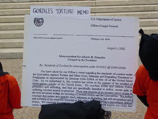 On a sign labeled "Gonzales Torture Memo" is an enlarged version of the first page of a memorandum for Alberto Gonzales, dated August 1, 2002, regarding "Standards of Conduct for Interrogation under 18 U.S.C. §§ 2340-2340A".