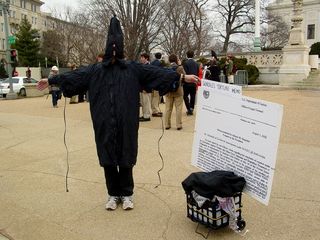 A man poses in a manner similar to a famous photo run by news organizations in order to remind those passing by of torture tactics used by our own military personnel.