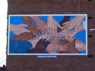 A mural is painted onto the bricks as a tribute to the Rev. Bev Cosby, a local minister, showing a laying of hands of people associated with Cosby. This mural, according to information I've found, is the first of a series that Lynchburg has planned for downtown.