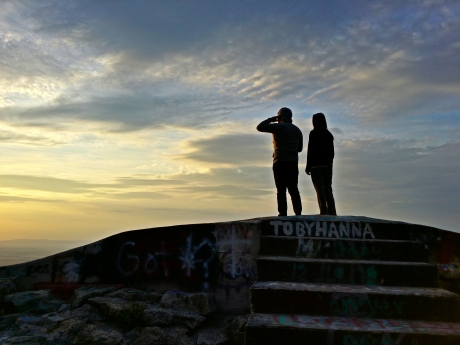 A man and a woman stand on High Rock, while the man talks on his phone.