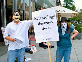 A man gives rabbit ears to a sign critical of the Church of Scientology.
