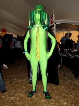 A man in a green zentai suit and various accessories makes the rounds through the sponsor tent.