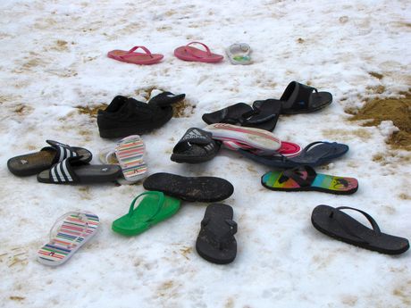 A bunch of abandoned flip-flops in a pile on the beach.