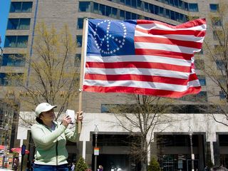 A woman holds up a US flag, where the fifty stars are arranged to form a peace sign