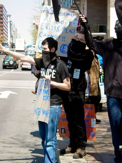 At the corner of 14th Street and Pennsylvania Avenue, just outside the JW Marriott Hotel, a black bloc has assembled. Here, two of these masked protesters, which you may recall are the ones we encountered earlier, are holding up their signs in front of 14th Street traffic. One of the most memorable things to happen while covering the black bloc was when a man riding in a passing car yelled out the window, "Why don't you love America?"
