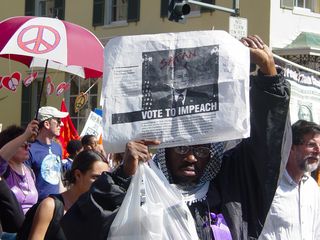 This man holds up a sign saying "Vote To Impeach", with Bush decorated up not as Hitler, but rather as the spawn of Satan.