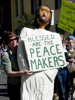 Another protester holds up a large sculpture of Jesus, holding a sign saying "Blessed are the peacemakers".