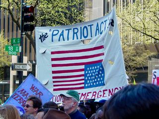 Other familiar scenes make their appearance, as the Patriot Act banner and corporate logo flag finish the protest route.