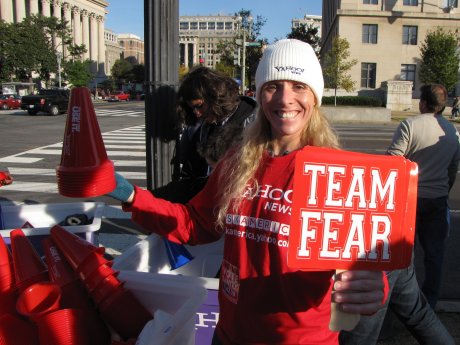 A woman hands out red "TEAM FEAR" signs and bullhorns.