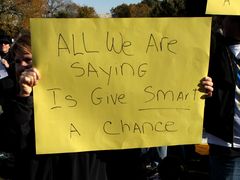 A woman holds a sign reading, "All we are saying is give smart a chance."