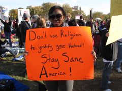 A woman holds a protest sign encouraging sanity by not using religion to justify hatred.