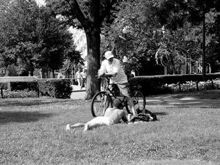 On the other side of the park, another man takes a moment to sunbathe, and also speak to a bicyclist passing by.