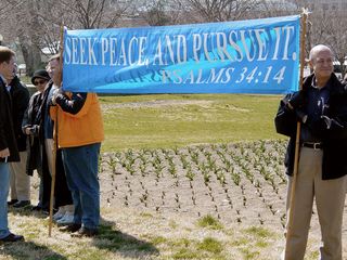 Meanwhile, just beyond a retaining wall, a small but determined group of people holds a silent vigil in protest of the occupation of Iraq on the year anniversary of the US invasion.