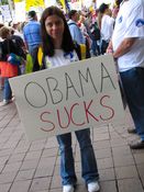 A woman holds a poster with the straightforward message, "Obama Sucks".