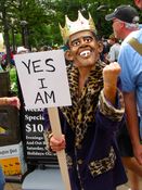A woman wearing an Obama mask (with cigarette danging from the mouth) depicts President Obama as a king with the sign, "Yes, I am".