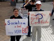 A woman holds a sign denouncing socialism, while a man holds a sign questioning President Obama's citizenship.