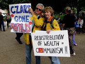 A couple holds their protest signs. The man's sign says, "Czars gone wild", while the woman's sign equates redistribution of wealth with communism.