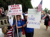 Two women hold signs, with one advocating term limits for politicians, while another denounces manmade climate change.