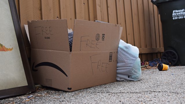 Amazon box along a fence containing items that are designated as being free for the taking.