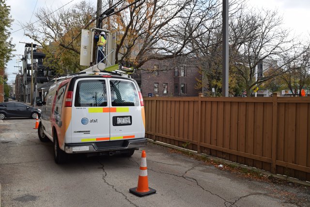 A workman maintains telephone equipment in a box mounted high up on a utility pole.