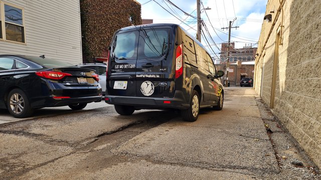 A utility van crosses a speed hump while traveling westbound through the alley.