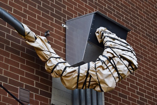 A cluster of cables leading from a nearby utility pole is wrapped at the point where it attaches to a box on the side of an apartment building.