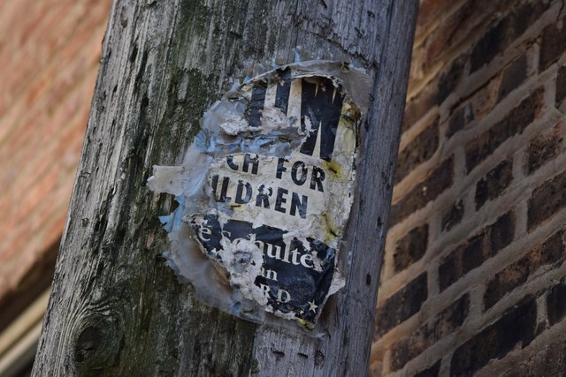 A very weathered poster on a utility pole in the alley south of West Leland Avenue, containing a combination of a "Slow, watch for children" sign, and some sort of political advertisement.